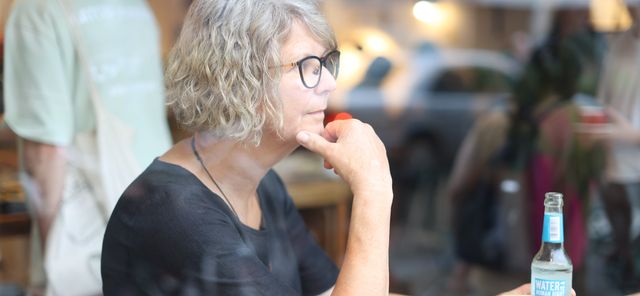 Susanne Menge sitzt in einem Café, mit nachdenklichem Gesichtsausdruck